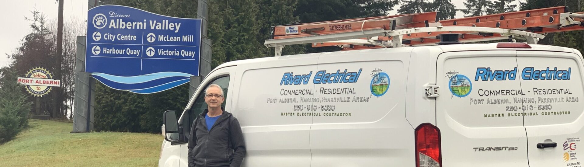 Jim Rivard, electrician servicing Port Alberni, Nanaimo and Parksville stands in front of his electrical van near the Port Alberni sign. He looks friendly and knowledgable.